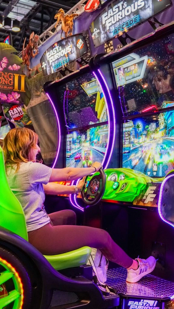 Players sitting and playing on premium Kuliku arcade machines in a vibrant game center with claw machines and redemption games